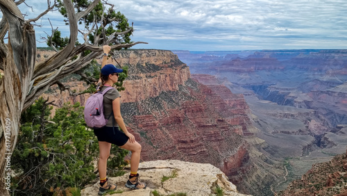 Woman next to old dry tree with scenic aerial view from Skeleton Point on South Kaibab hiking trail, South Rim, Grand Canyon National Park, Arizona, USA. Colorado River weaving through rugged terrain