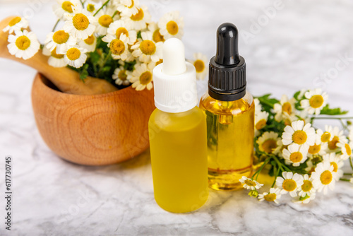 Chamomile essential oil.Glass bottle with chamomile essential oil on a marble background. Chamomile flowers, close up. Aromatherapy, spa and herbal medicine ingredients. Space for copy. Beauty concept