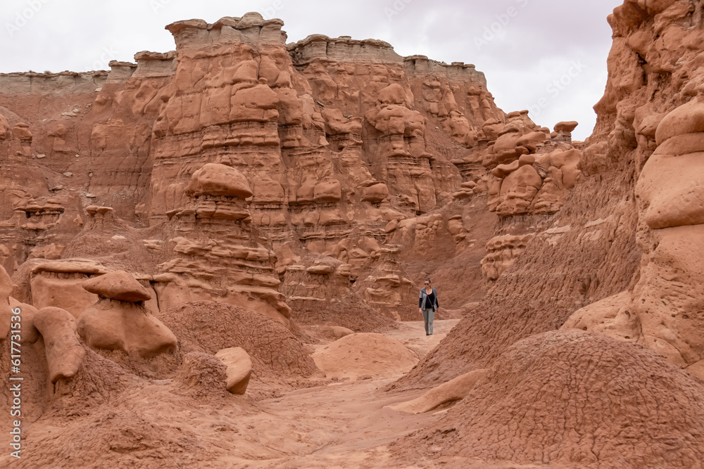 Woman hiking next to unique eroded Hoodoo Rock Formations at Goblin Valley State Park in Utah, USA, America. Sandstone rocks called goblins which are mushroom-shaped rock pinnacles. Canyon hike trail
