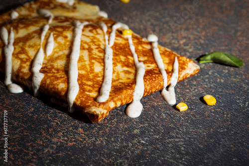 Side view of delicious salty pancake with filling and sauce against dark textured background