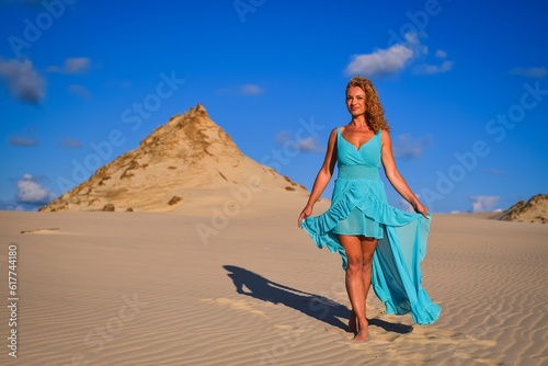 Beautiful blonde woman on hot sand with blue sky in the background. Photo taken on the shifting dunes over the Baltic Sea in Leba, Poland. Photo with a shallow depth of field with blurred background.