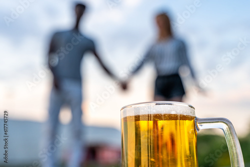 Foto close-up of a glass of beer in front of a multiracial couple of lovers blurred i