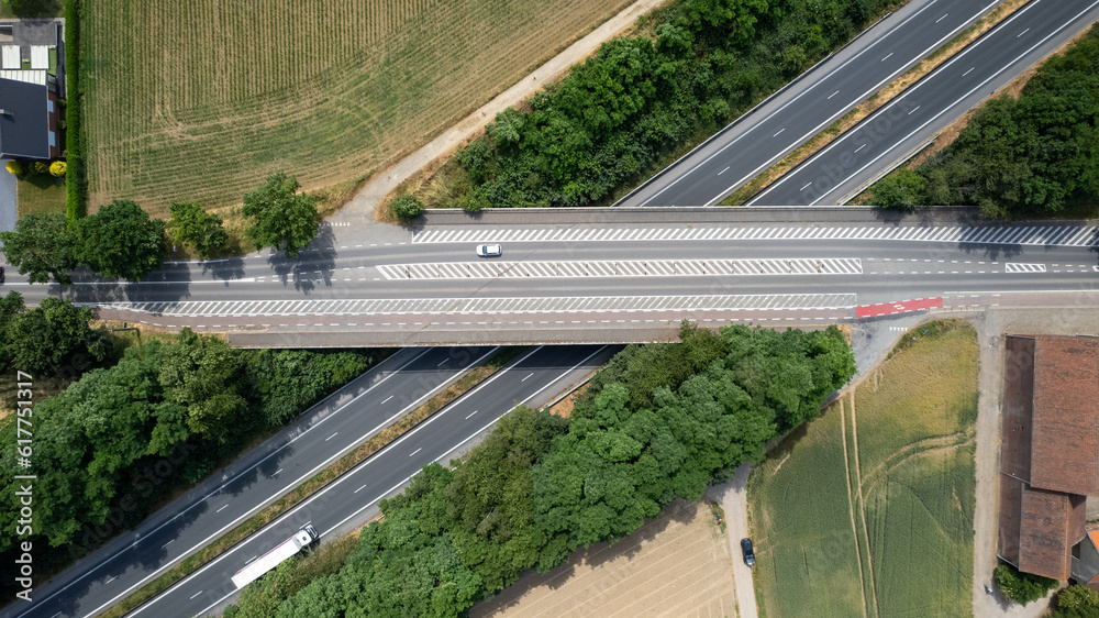 Aerial view of the road with bridge over a highway and forest and fields next to it on a summer sunny day. Highway in Belgium. High quality photo