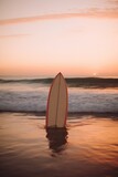 Orange and white surfboard standing on beach at sunset, created using generative ai technology