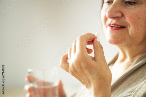 Close up of a retired woman in casual clothes at home holding pill and glass water. 