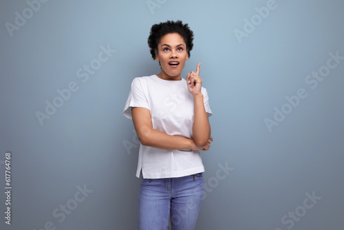 a young brunette woman with afro hair in a white t-shirt demonstrates with inspiration with the help of her hands an advertisement