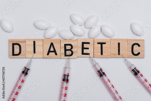 Napis diabetyk ułożony na białym tle, obok strzykawki insulinówki i lekarstwa 