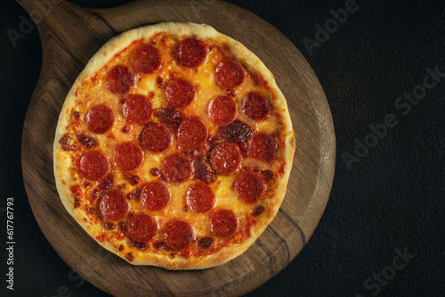 An uneven and slightly burnt homemade pepperoni pizza on a wooden tray on the table. Copyspace