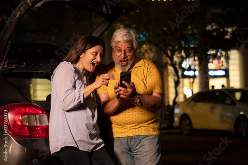 Happy senior citizen couple at night in market using mobile phone