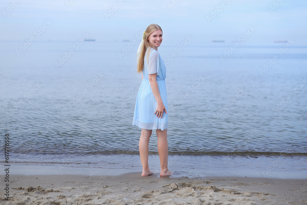 amazing girl in a blue dress with a beautiful sports body walking and posing on a white sand beach. 