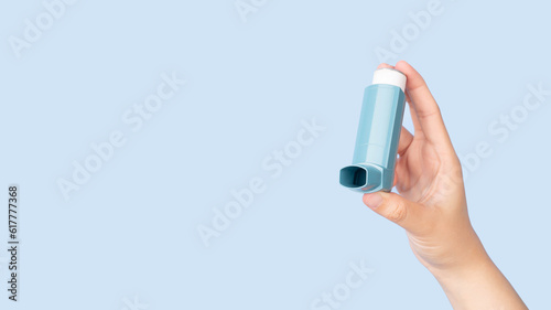 Hands holding asthma inhaler for relief asthma attack isolated blue background. Pharmaceutical products is used to prevent and treat wheezing and shortness of breath caused asthma or COPD. photo