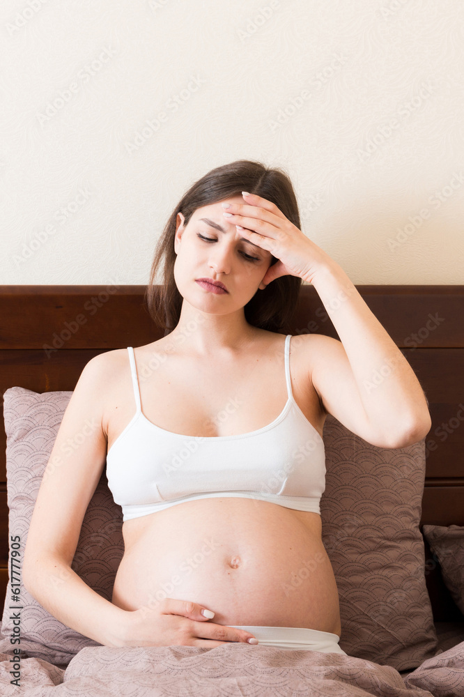 Young pretty pregnant woman suffering from headache at home in bed Young pretty pregnant woman suffering from headache at home in bed
