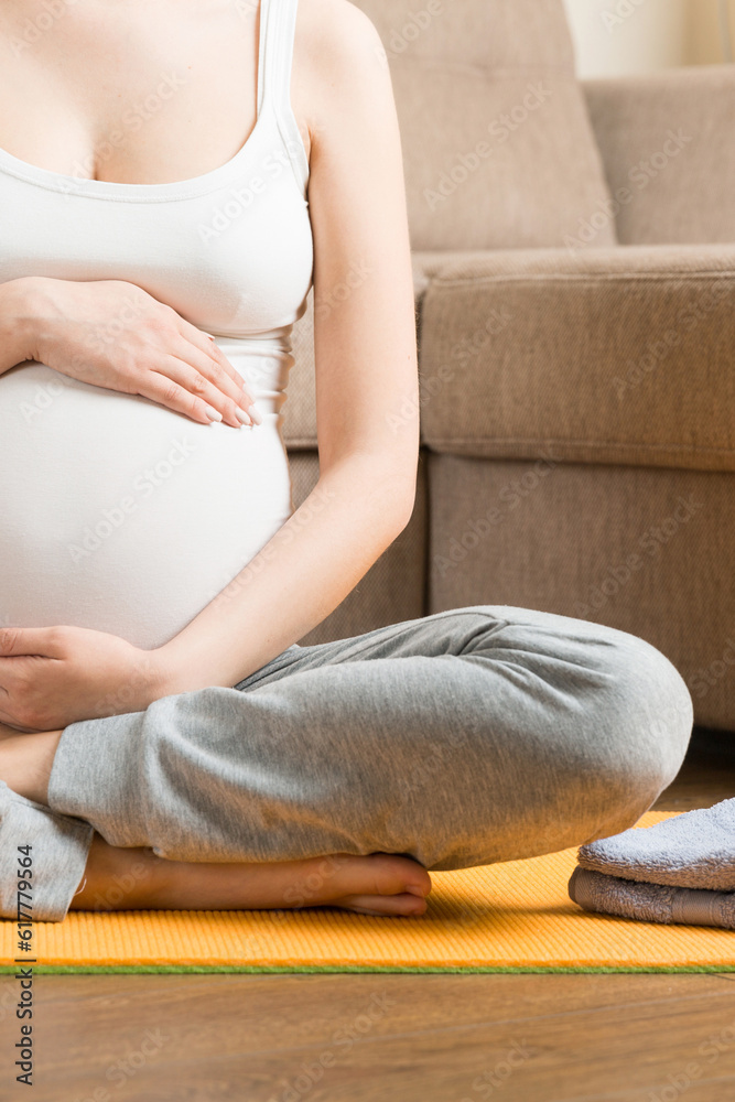 Pregnant young woman with bottle of water while sitting in lotus position on yoga mat. Maintaining water balance at coronavirus time