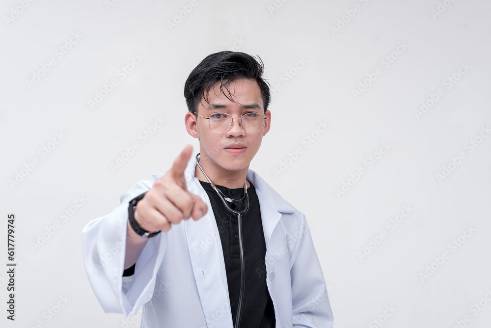 Portrait of a young and professional doctor, medical student, intern, pointing his finger towards the camera looking serious. Isolated on a white background.