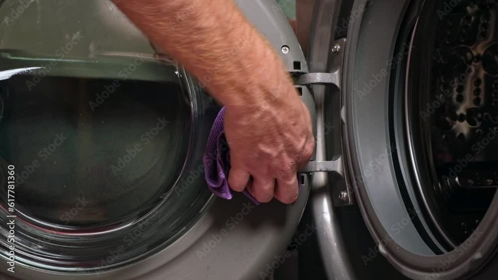Cleaning of the washing machine. A man wipes the door, the rubber band of the washing machine with a rag.