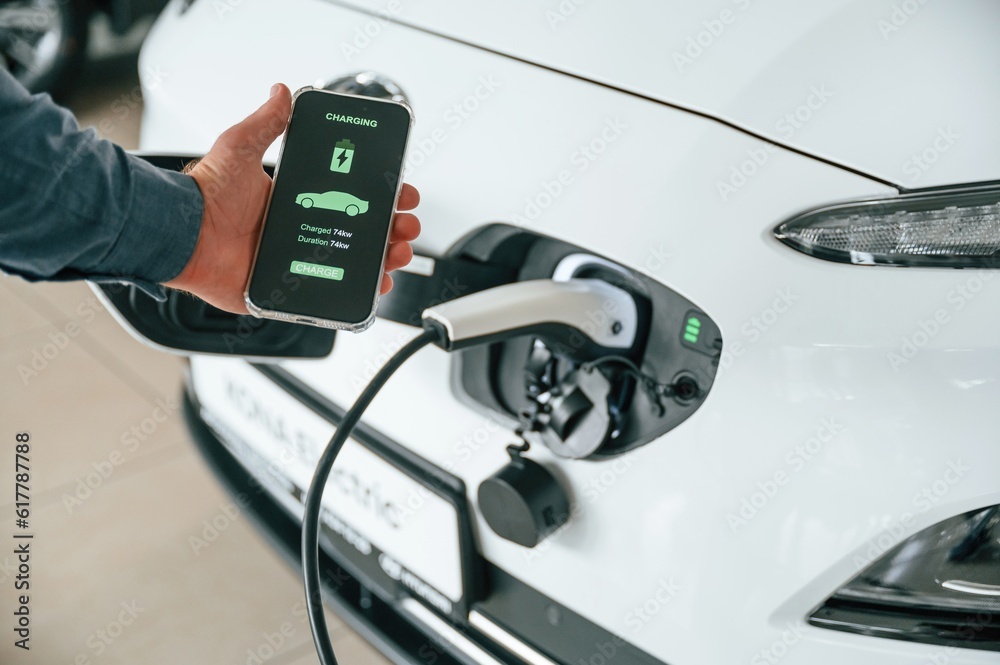 Using smartphone app for monitoring charging process. Close up view of man that is with electrical car Using smartphone app for monitoring charging process. Close up view of man that is with electrical car