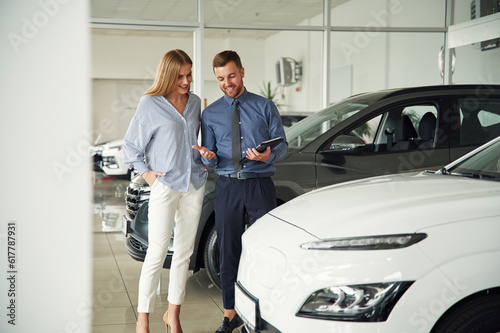 Choosing the automobile. Man in formal clothes is with woman customer with the electric car