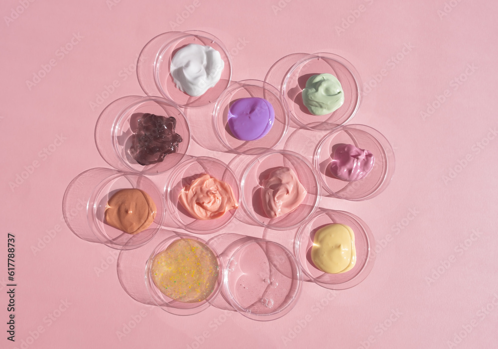 Multicolored textures of cream, scrub, serum and gel in Petri dishes on a pink background. Concept of cosmetics laboratory researches. Smear of skincare cosmetics product. Wellness and beauty concept.