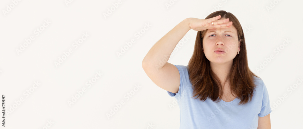 Portrait of curious woman in blue t-shirt holding hand above eyes and peering into distance, looking far away, expecting and searching someone on horizon
