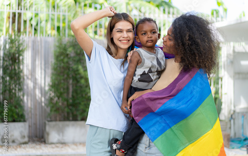 Lesbian couple playing rainbow flag with little child. Multiethnic woman and family happy leisure together outdoor. Diversity gay women, homosexual, LGBT, same gender mariage motherhood lifestyle. © Nassorn