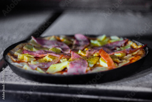 Very complete deliciously italian homemade pizza entering a wood-fired oven for baking.