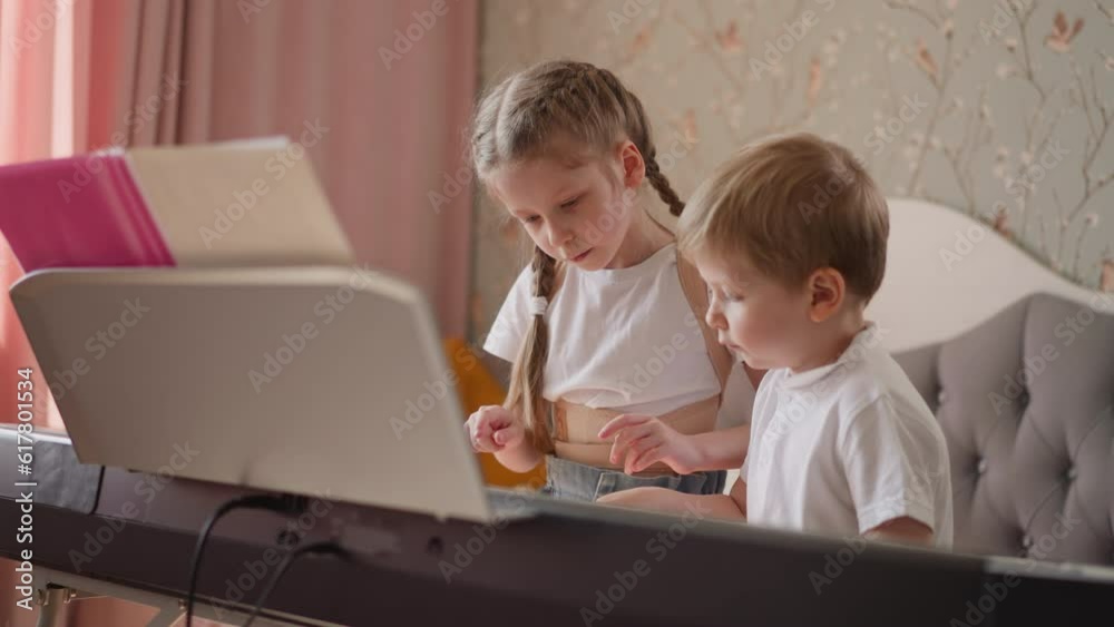 Little girl takes brother hand and presses electric piano keys at home lesson. Cute children learn music playing with modern digital instrument Little girl takes brother hand and presses electric piano keys at home lesson. Cute children learn music playing with modern digital instrument