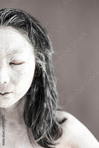 Art portrait of asian woman covered in clay isolated over grey background. Woman face like cracked pottery cup holding by hand.
