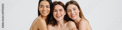 Three happy smiling girls hug and pose in studio isolated