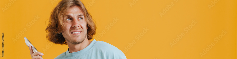 Fototapeta premium Young confused man wearing t-shirt gesturing and using cellphone