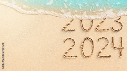 New Year concept banner of coming 2024. Numbers 2023 handwritten in sand, tropical beach background with soft blue ocean wave and copy space for your design or text