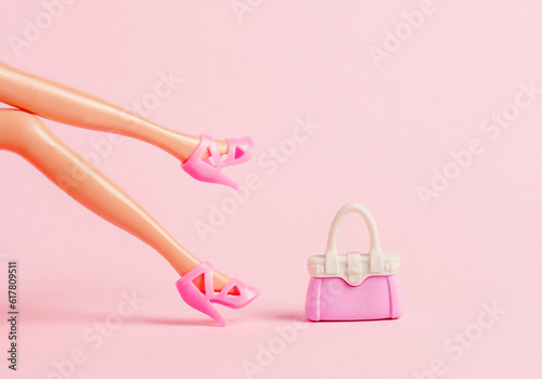 Plastic toy legs with high heels and little bag on pastel pink background. Minimal art pink poster. photo