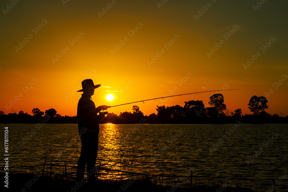 Silhouette sunset of a fisherman with a fishing rod at lake.