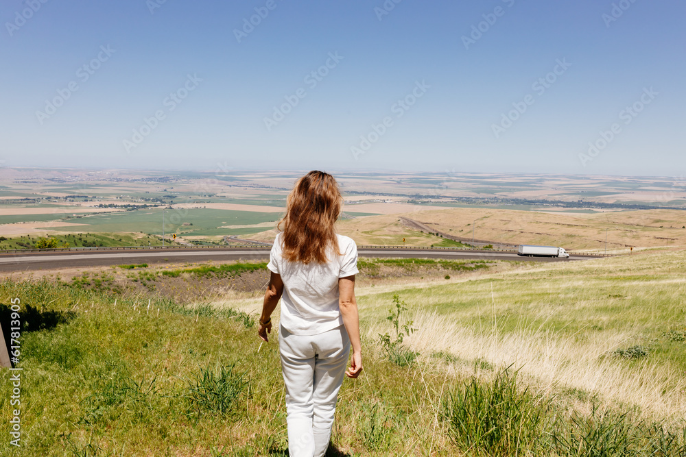 Beautiful summer landscape with meadows and a road from a bird's eye view. Nature in Oregon. A girl in sportswear with red hair walks in a summer meadow, rests in nature, admires nature