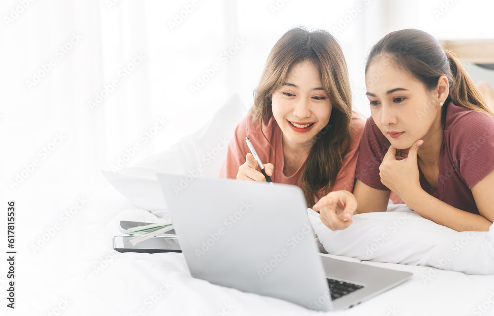 Asian women couple living together, lying on a white bed, using a laptop for rest.