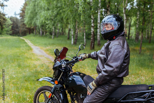 Senior motorcyclist riding motobike outdoors. Man in leather jacket resting after ride in summer forest. Space