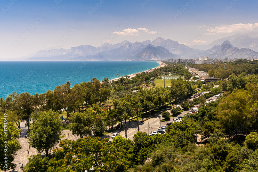 Aerial view of scenic and popular Konyaalti beach in Antalya resort town. Majestic mountains with sunset haze in the background. Vacation and holiday in Turkey