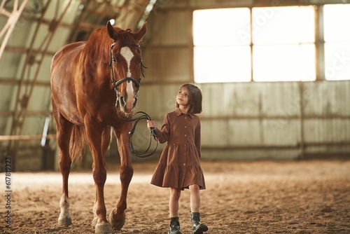 Holding animal, walking together. Cute little girl is with horse indoors