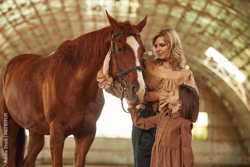 Woman with her little daughter is with horse indoors © standret