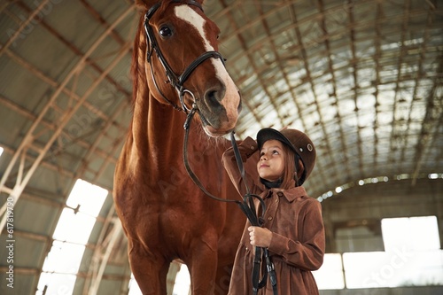 In jockey clothes. Cute little girl is with horse indoors © standret