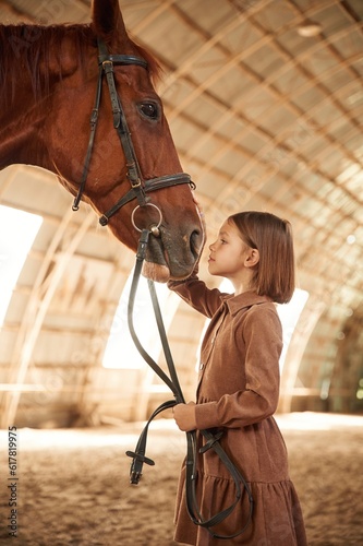 Touching the head of animal. Cute little girl is with horse indoors