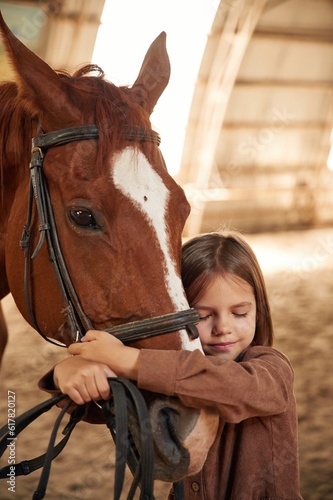 Embracing the animal. Cute little girl is with horse indoors