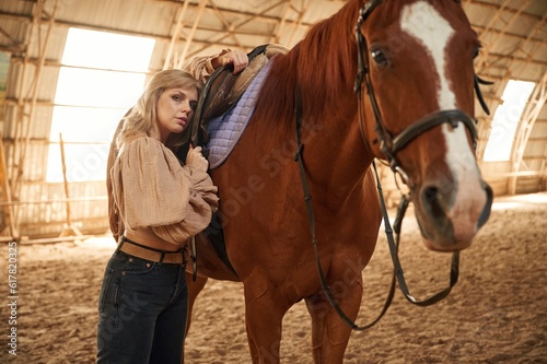 Taking care of animal. Beautiful young woman is with horse indoors