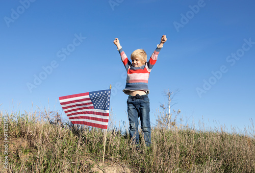 boy proudly raised his hands, an American flag stands nearby, focus on the flag. Celebration of Independence Day of the United States of America. Pride, happiness, success, freedom, national symbol