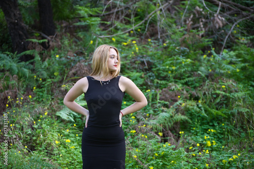 Young, beautiful blonde woman dressed in black walks through the forest in different postures and expressions. In the background ferns and yellow flowers. Concept expressions in nature.