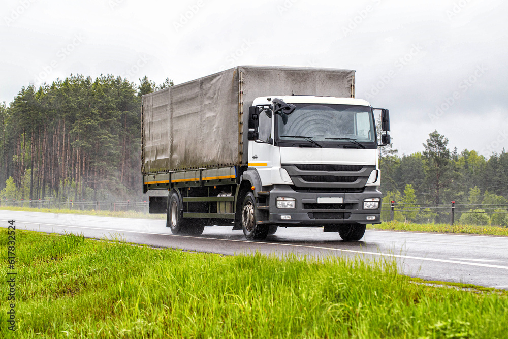 A tilt truck transports cargo on a highway in rainy weather on a slippery road. The concept of import substitution. Copy space for text
