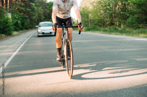 A cyclist in gear rides along an asphalt road outside the city together with cars. © bodnarphoto