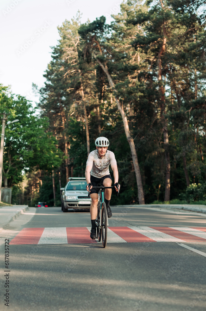 Fototapeta premium Positive young male cyclist riding a road bike on an asphalt road outside the city and smiling. Vertical photo.