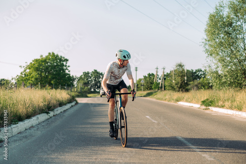 Sportsman male cyclist in gear rides a road bike outside the city on roads for cars. © bodnarphoto