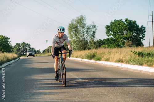 A sporty active man in gear walks on a road bike outside the city on roads for cars.