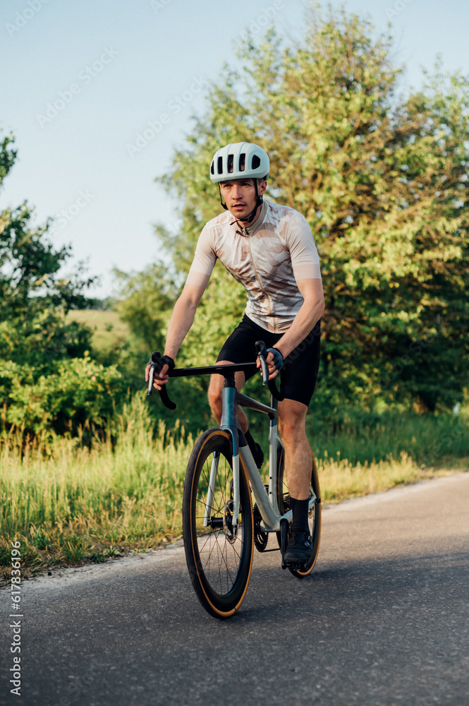 Obraz premium Photo of a male professional cyclist in sports equipment riding a road bike outside the city on an asphalt road. Vertical